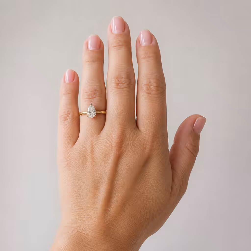 Mano pequeña con dedos cortos usando un anillo de compromiso con piedra pera y banda fina.