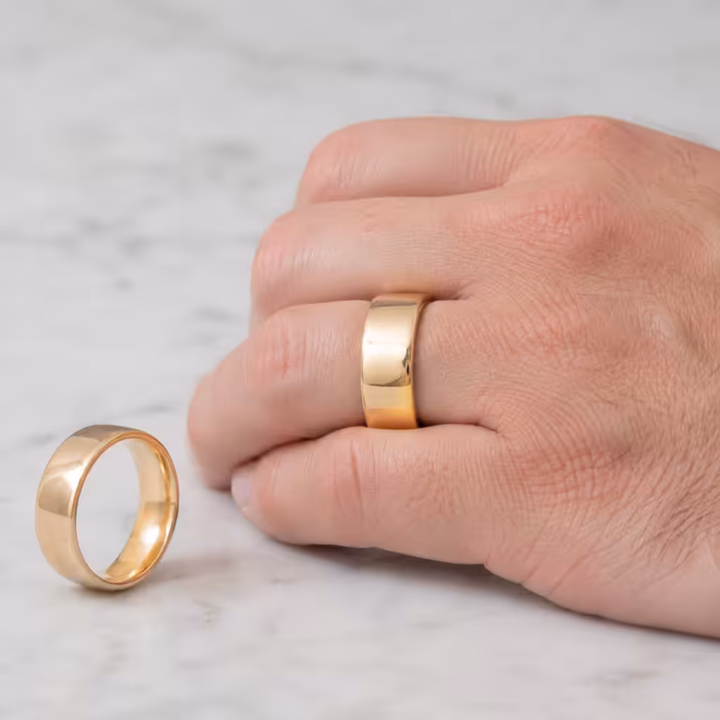 Argolla de matrimonio ancha de oro amarillo en una mano adulta.