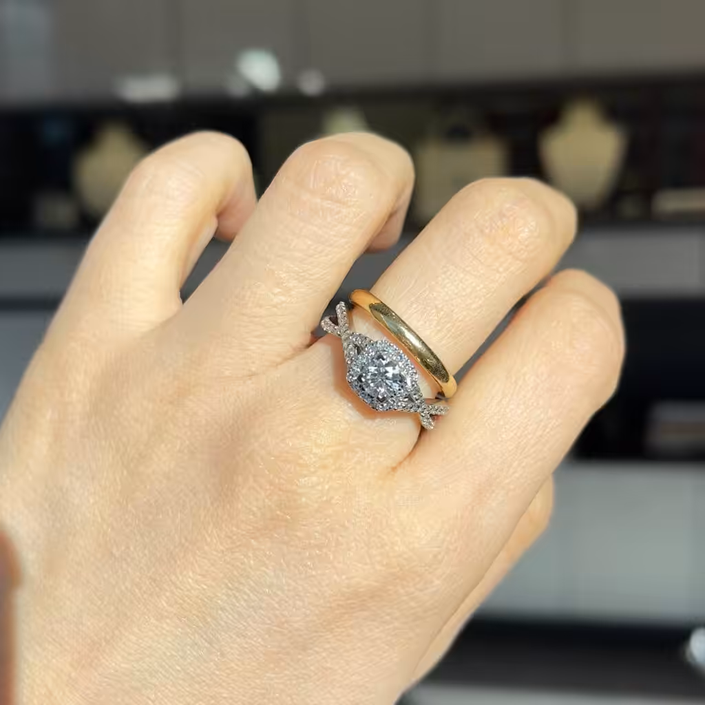 Anillo de compromiso con halo y argolla de matrimonio clásica puestos juntos sobre una mano.