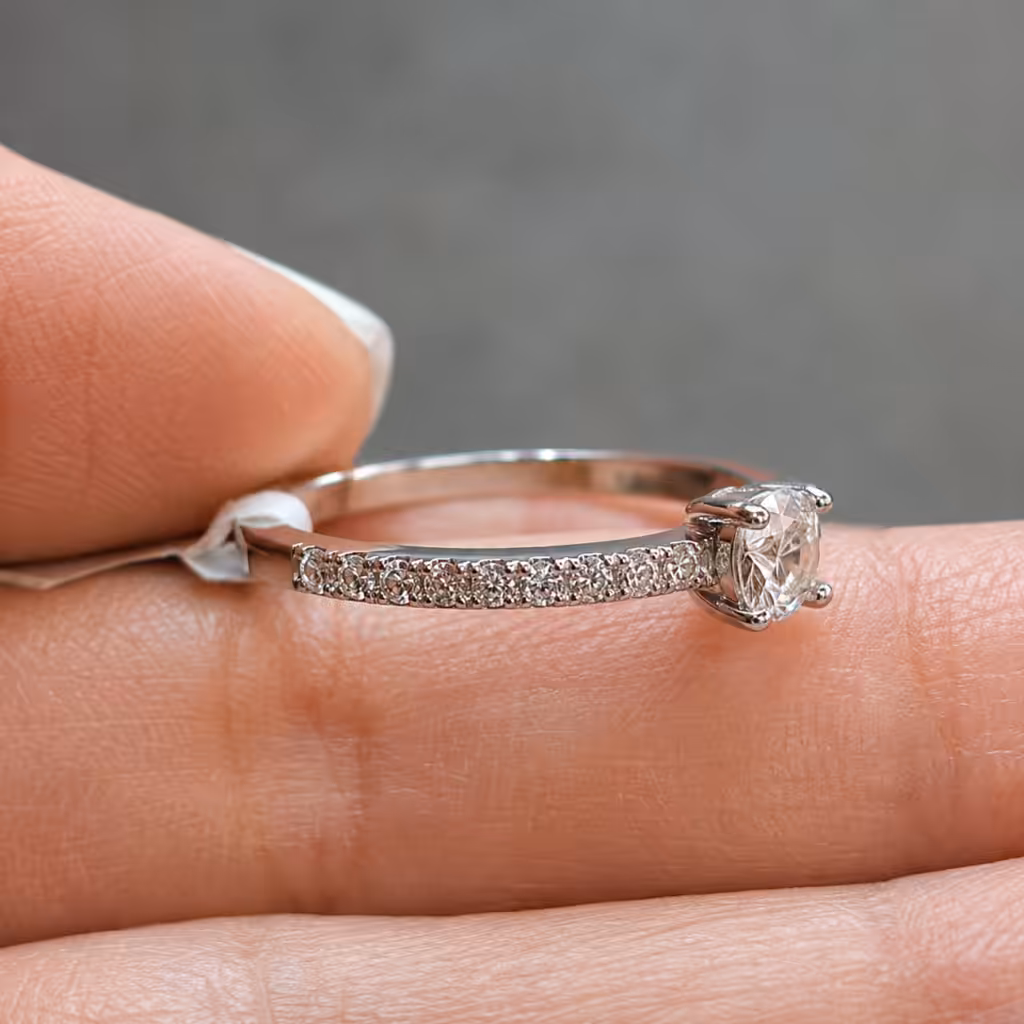 Solitario con diamante central y pavé visto de lado sobre una mano.